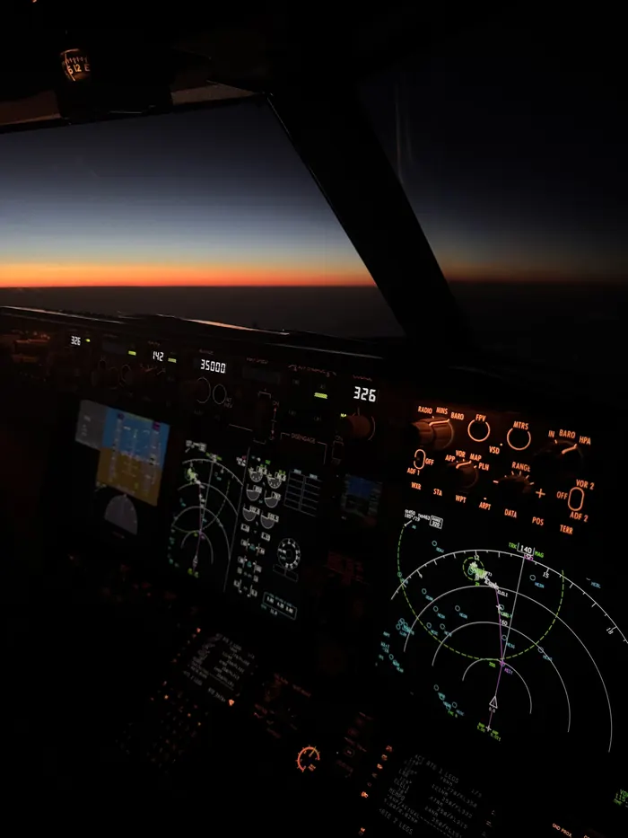 Kokpit Boeingu 737 při soumraku, na obzoru oranžový pás světla